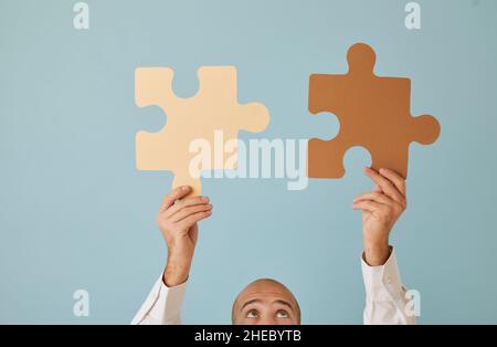 Man holding and joining brown and beige jigsaw puzzle pieces that match perfectly Stock Photo