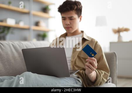 Focused asian guy showing using credit card at home Stock Photo