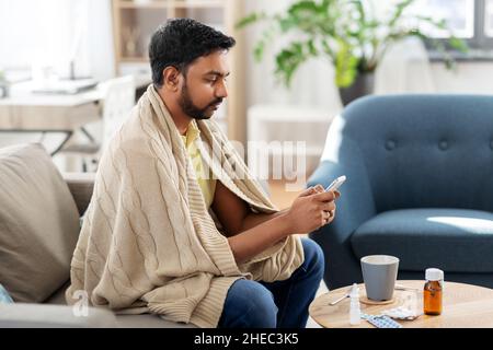 sick young man in blanket with smartphone at home Stock Photo