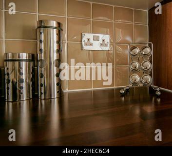 Stainless steel chrome storage containers on a modern kitchen worktop, taupe coloured tiles, chrome electrical socket. Stock Photo