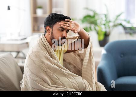 sick young man in blanket having headache or fever Stock Photo