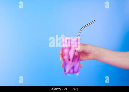 Female hand with pink cold refreshing cocktail in glass on blue background. Summer drink background with copy space. Stock Photo