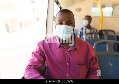 African american businessman wearing a face mask sitting on the bus while on the go to office Stock Photo