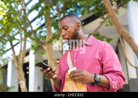 African american businessman having a snack and using smartphone while on the go to office Stock Photo