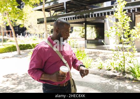 African american businessman holding a coffee and using smartwatch while on the go to office Stock Photo