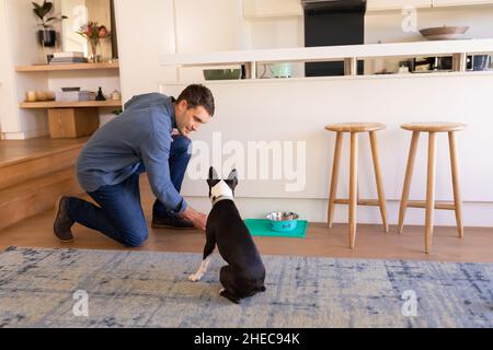 Caucasian man feeding his dog in the living room at home
