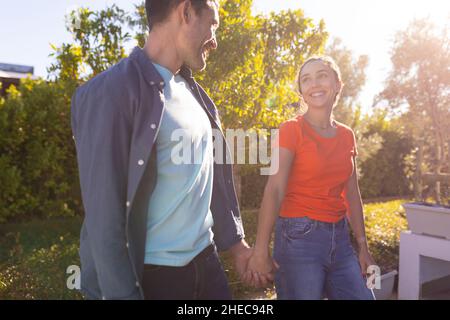 Caucasian couple holding hands smiling looking at each other while walking in the garden Stock Photo
