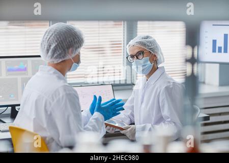 Two scientists in protective workwear talking to each other during their work in the laboratory Stock Photo