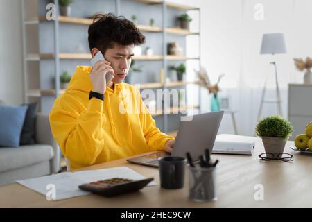 Serious asian man working and talking on phone at home Stock Photo