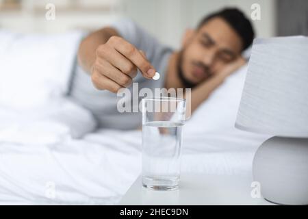 Arab Man Putting Pill Into Glass Of Water Standing On Bedside Table Stock Photo