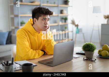 Bored Asian male student sitting at desk with pc Stock Photo
