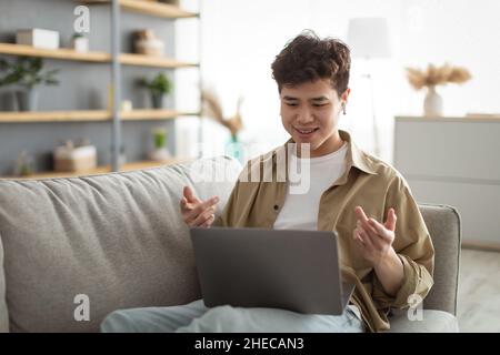 Asian man having videochat using laptop and talking at webcam Stock Photo