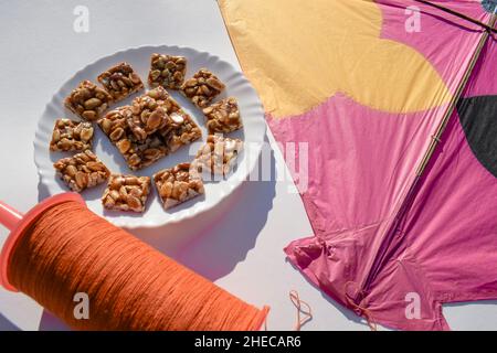 Peanut chikki or Moongfalli chikky bars with Kite and spool string with white background. Makar sankranti, uttarayan, pongal, Lohri festival posters f Stock Photo