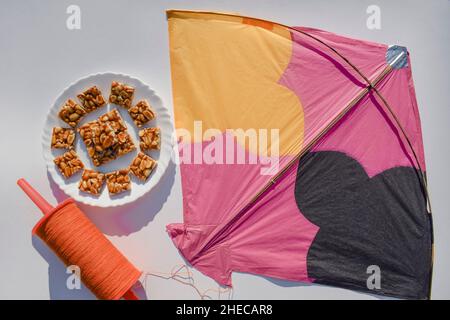 Peanut chikki or Moongfalli chikky bars with Kite and spool string with white background. Makar sankranti, uttarayan, pongal, Lohri festival posters f Stock Photo