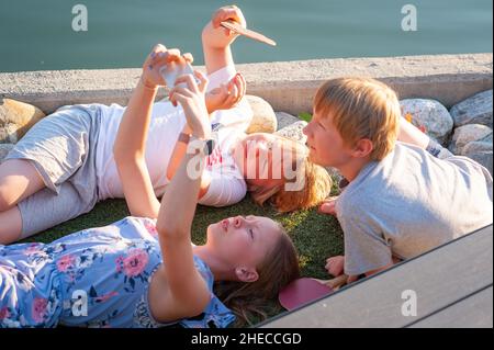 Kids with smart phones out on the deck by the sea enjoying warm sunlight, Eidfjord, Norway Stock Photo
