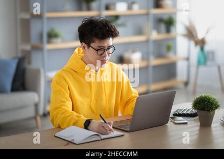 Smiling asian man working on laptop and writing Stock Photo
