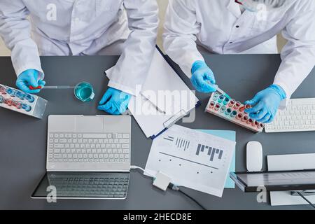 High angle view of scientists holding scientific experiment at the table with blue liquid in test tubes in the laboratory Stock Photo