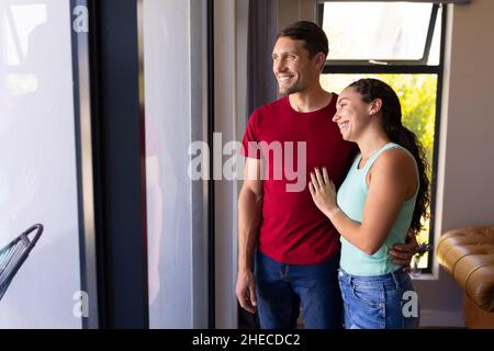 Happy caucasian couple looking out of the window at home Stock Photo