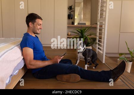 Caucasian man smiling while using smartphone sitting on the floor at home Stock Photo