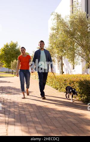 Happy caucasian couple holding hands and walking their dog outdoors Stock Photo