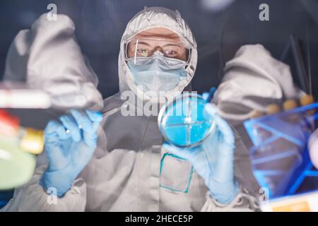 Low angle view of doctor in protective suit analyzing samples in tube during research in the lab Stock Photo