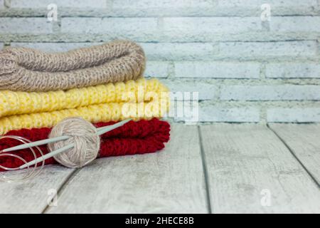 folded multi-colored knits with a ball of thread and knitting needles on a light wooden background. handicraft concept, sale Stock Photo