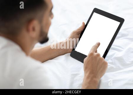 Arab Man Using Digital Tablet With Blank Screen While Lying In Bed Stock Photo