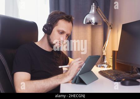 Front view of happy man with headphones using a tablet sitting in a coffee shop or home Stock Photo