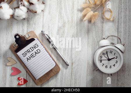 SPRING AHEAD text on notepad rustic wood flat lay with hearts, alarm clock, and natural elements.  Daylight Saving Time concept. Stock Photo