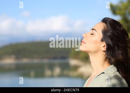 Side view portrait of a relaxed woman breathing fresh air in a lake a sunny day Stock Photo