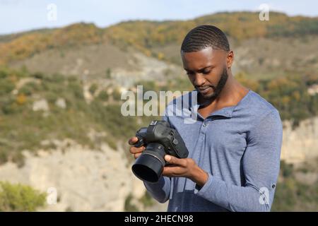 Concentrated man with black skin checking photos on dslr camera in nature Stock Photo