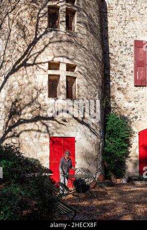 France, Herault, Pezenas, elderly woman in front of the facade of an old rural historic building Stock Photo