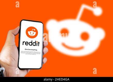 San Francisco, USA, December 2021: Hand holding a phone with Freshworks mobile application on the screen. Reddit logo blurred on an orange background. Stock Photo
