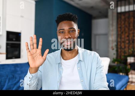 Video call. Cheerful attractive African-American guy using computer app for video communication, smiling guy looking and waiving into the camera, greeting, talking online. Webcam view of participant Stock Photo