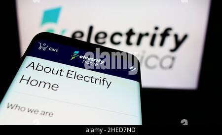 Mobile phone with webpage of American EV charging company Electrify America LLC on screen in front of logo. Focus on top-left of phone display. Stock Photo