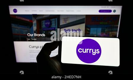 Person holding smartphone with logo of British electronics retail company Currys plc on screen in front of website. Focus on phone display. Stock Photo