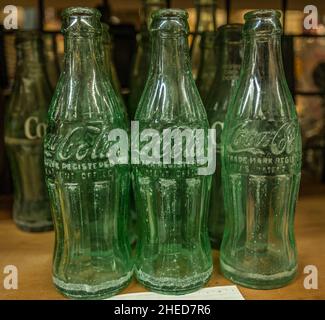 Several antique Coca-Cola glass bottles together display on a shelf in a row closeup Stock Photo