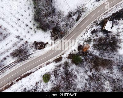 High angle top down aerial view drone image on road trough the trees and forest in mountain range covered with white snow in winter day near Knjazevac Stock Photo