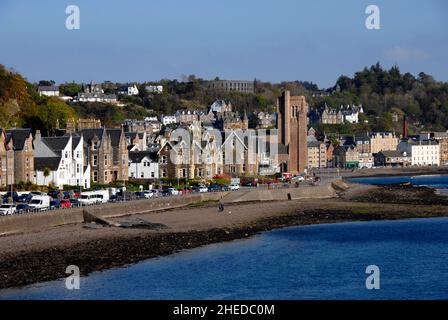 Oban seafront with vehicles parked nose to tail all along, Scotlamd. McCaig's Tower and Battery Hill are seen beyond Stock Photo