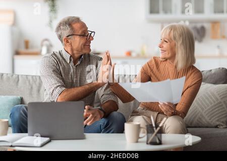 Mature Couple Holding Papers And Giving High-Five Reading Bills Indoors Stock Photo