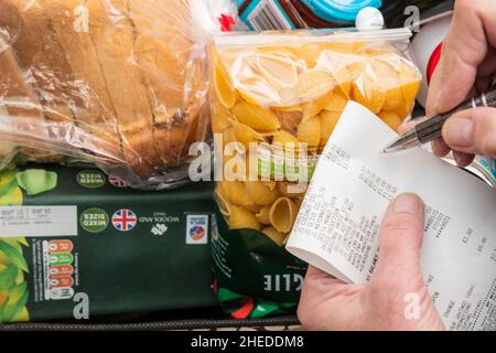 Woman checking her groceries against a supermarket till roll - budgeting to reduce her cost of living. Stock Photo