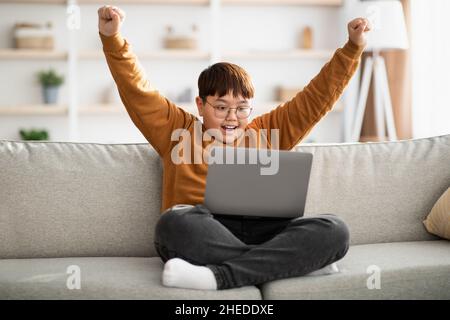 Happy teenager looking at computer screen and raising hands up Stock Photo