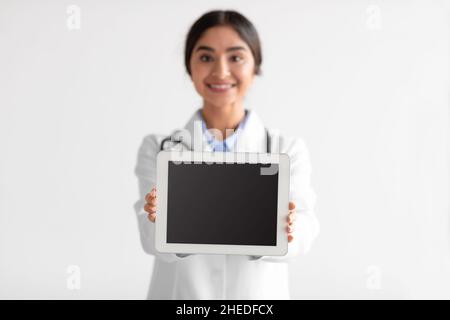 Smiling millennial hindu woman nurse or doctor in uniform shows digital tablet with empty screen Stock Photo