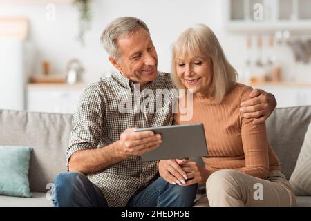 Senior Spouses Watching Movie On Tablet Embracing Sitting At Home Stock Photo
