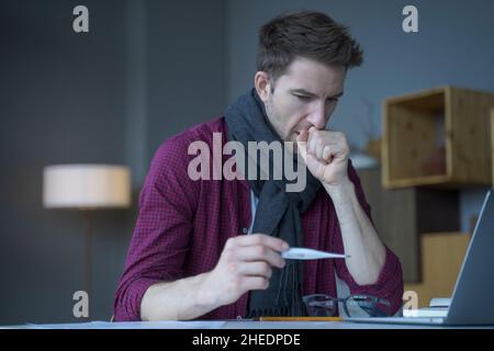 Unhealthy looking male entrepreneur in scarf around his neck coughing looks at digital thermometer Stock Photo