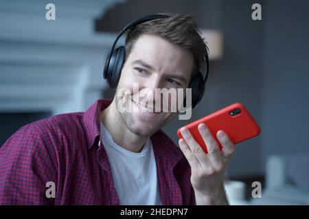 Smiling young German man in headphones recording voice message for collegue, using speakerphone Stock Photo
