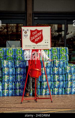 10-03 2021 Tulsa OK USA - Salvation Army bellringer (face hidden) in front of stacked packages of water bottles with hanging kettle on sidewalk at sto Stock Photo