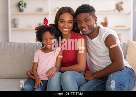 Coronavirus Vaccination. Vaccinated Black Family With Plaster On Arms Posing At Home Stock Photo