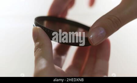Close up of polarizing lens filter in girls hands isolated on white background. Woman turning into the both sides mechanism of lens filter. Stock Photo