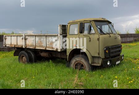 An old lorry in a field among the green grass. Military cabin color. Rusty body. Stock Photo